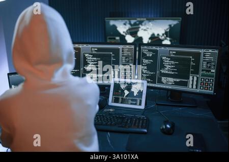Young professional female hacker is indoors by computer with lot of information on displays. Stock Photo