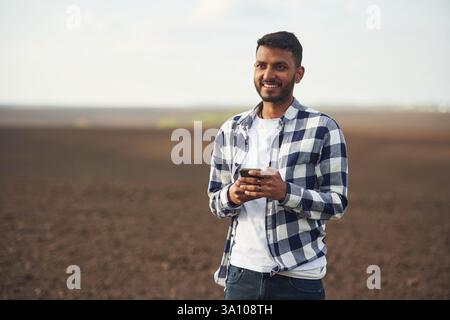 Smartphone in hands. Cultivated agricultural field. Handsome Indian man. Stock Photo
