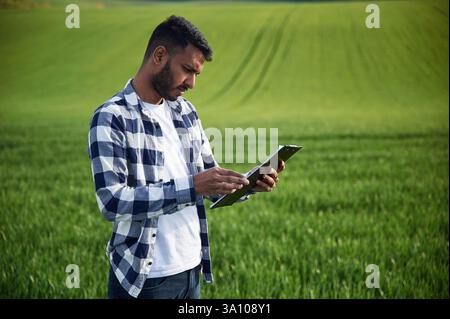 Reading the information from notepad. Handsome Indian man is on the agricultural field. Stock Photo