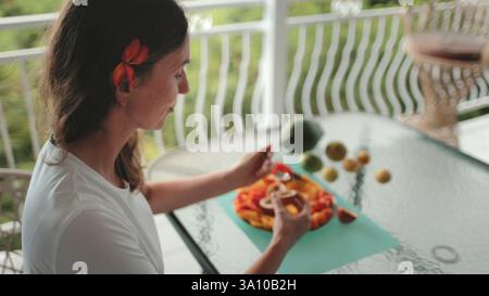Tourist is enjoying a tropical breakfast on a balcony with a view of the lush greenery. She is savoring a plate of fresh papaya and other exotic fruits, creating a vibrant and appetizing scene Stock Photo