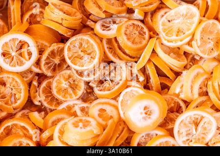 Dense arrangement of candied lemon slices with translucent centers and crystallized sugar coating forming a textured background with bright yellow and Stock Photo