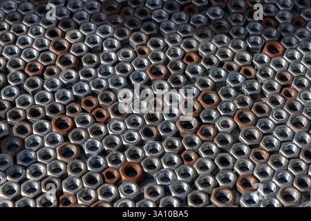 Background of metal hex nuts arranged in a dense pattern reflective silver surfaces contrast with rusted elements creating an industrial composition Stock Photo