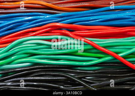 Background of multicolored candy ropes arranged in parallel layers with glossy smooth surfaces in red blue green black and brown shades forming a vibr Stock Photo