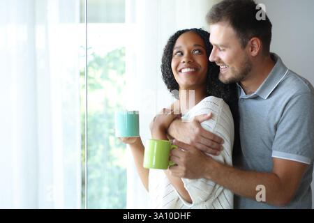 Happy interracial couple drinking and looking each other at home Stock Photo