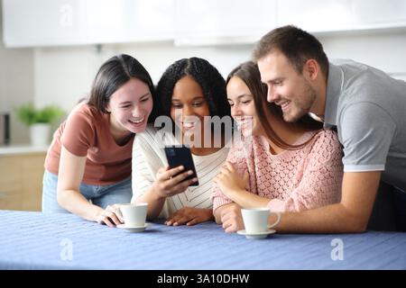 Happy interracial group of friends checking phone in the kitchen at home Stock Photo