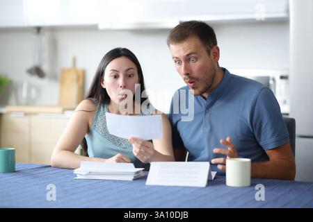 Surprised interracial couple checking bank statement in the kitchen at home Stock Photo