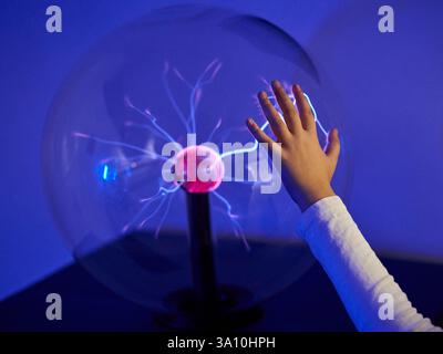 A child's hand touching a glowing plasma ball lamp creating electric filaments at the Museum of Illusions, Florence, Tuscany, Italy. Stock Photo