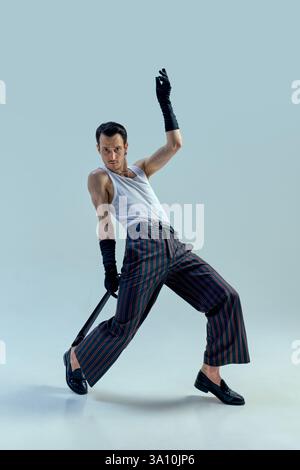 Dynamic performer striking powerful pose with intense gaze, gripping microphone in expressive dance motion against soft-toned studio background. Stock Photo
