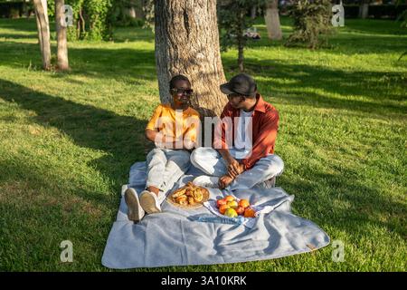Young black couple on blanket, eating and talking on park picnic. City escape and digital detox Stock Photo