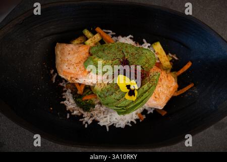 Top view of a Delicious and creative grilled salmon loin dish with white rice and avocado. It is decorated with a yellow flower and the plate and the Stock Photo