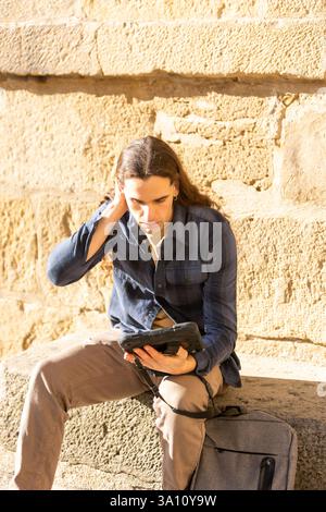 Traveler using a rugged tablet while sitting outdoors. Lifestyle, technology, tourism. Stock Photo