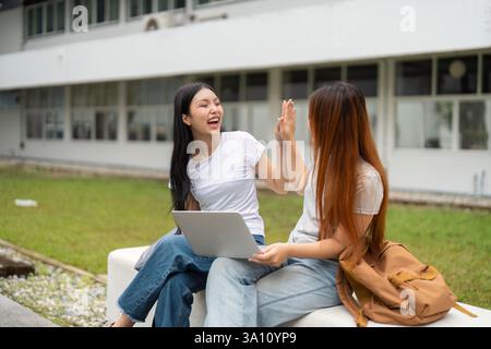 Two friends sharing a joyful moment outdoors, collaborating on a project with a laptop. Stock Photo