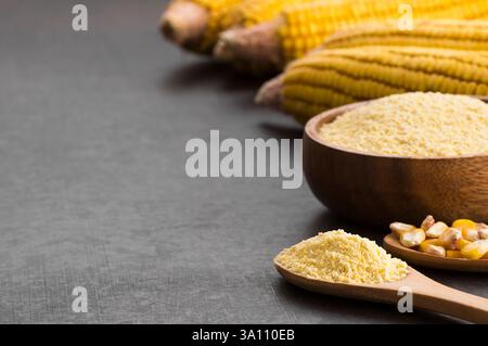 Corn flour in wooden bowl and spoon with dried corn groats, kernels on rustic table. corn ingredients concept Stock Photo