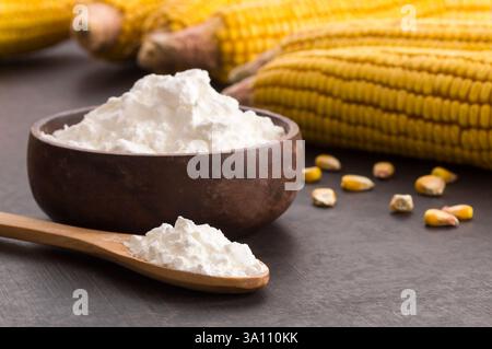 Corn starch in wooden bowl and spoon with dried corn groats, kernels on rustic table. corn ingredients concept Stock Photo
