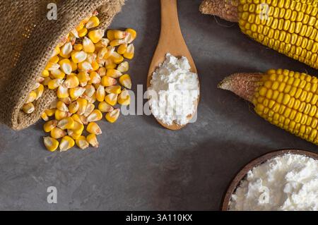 Corn starch in wooden bowl and spoon with dried corn groats, kernels on rustic table. corn ingredients concept Stock Photo