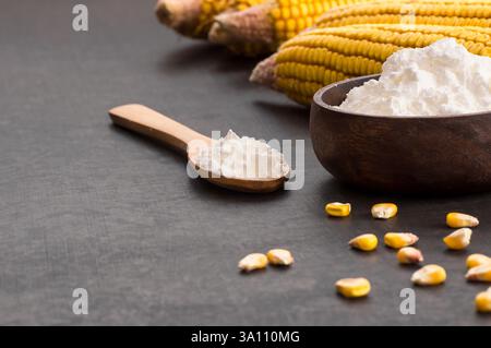 Corn starch in wooden bowl and spoon with dried corn groats, kernels on rustic table. corn ingredients concept Stock Photo