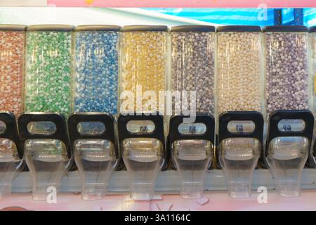 close-up shot of multiple clear dispensers filled with an array of colorful candies, including chocolate-coated bits, gummy pieces, and pastel mini be Stock Photo