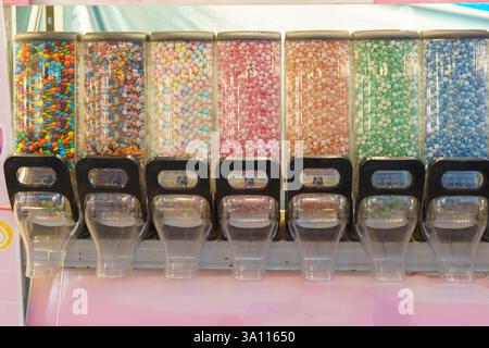 close-up shot of multiple clear dispensers filled with an array of colorful candies, including chocolate-coated bits, gummy pieces, and pastel mini be Stock Photo