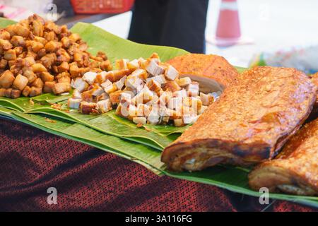 close-up shot of crispy pork belly slabs and fried pork bites neatly arranged on banana leaves at a street food stall. Stock Photo