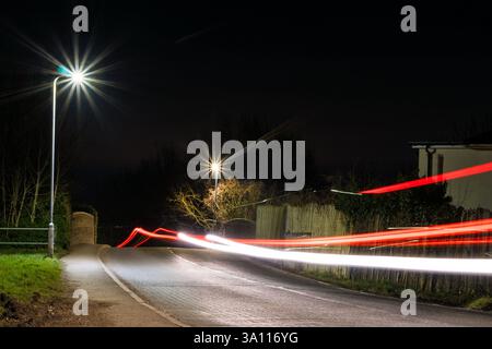 A road on the edge of the countryside with traffic trails and street lights at night Stock Photo