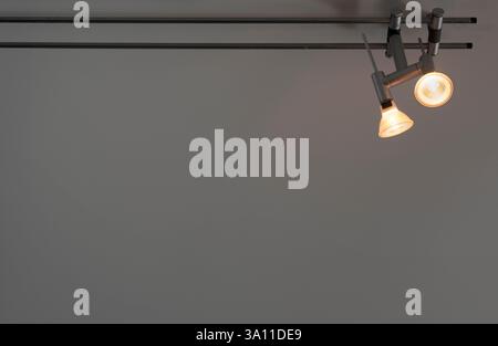 Two halogen or led spotlights on a rail. Space for text on the grey wall below Stock Photo