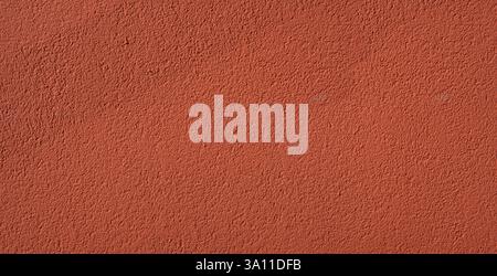 Background of red decorative plaster, with pits and grooves in random directions in the surface. Shined by the sun with shaded area Stock Photo