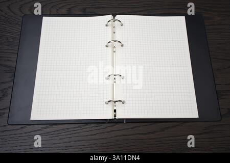black notebook with grid-lined pages is open on a dark wooden table. Stock Photo