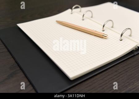 black notebook with grid-lined pages is open on a dark wooden table. Stock Photo