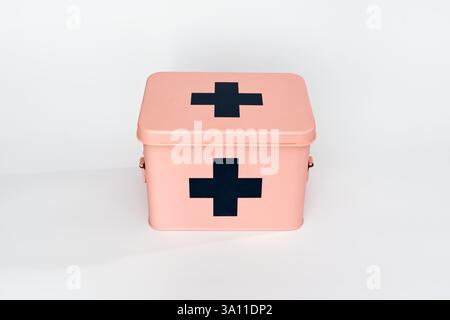 The image showcases a pink first aid box with black crosses on the top and front. It is positioned against a plain white background, emphasizing its c Stock Photo