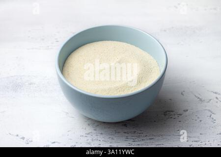 Light blue ceramic bowl filled with semolina sits on a textured light grey marble surface Stock Photo