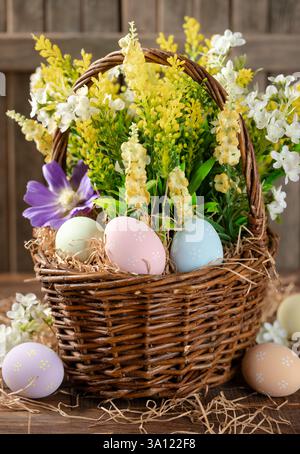 Easter eggs and flowers in a wicker basket  on a wooden table and background Stock Photo