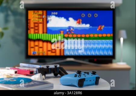 Milan, Lombardy, Italy - February 24, 2025: Blue gamepad playing a retro Sonic The Hedgehog platform videogame on a big television screen Stock Photo
