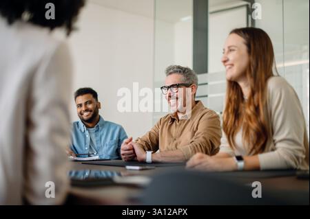 A diverse group of professionals in a business meeting, engaged in a conversation. The atmosphere is collaborative, with smiling faces and teamwork in a modern office. Stock Photo
