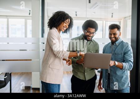 Three business professionals engaged in a discussion while reviewing data on a laptop in a modern office. A diverse team collaborating on corporate growth and business strategy. Stock Photo