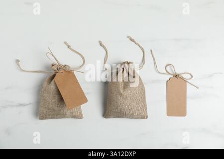 Burlap bags with tags on white marble table, flat lay Stock Photo