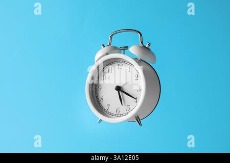 White alarm clock in air on light blue background Stock Photo