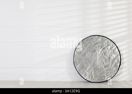 Professional reflector on floor near white wall, space for text. Photo studio equipment Stock Photo