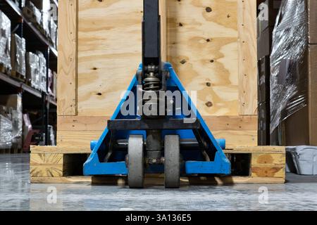 Blue pallet jack under wooden crate pallet ground level industrial warehouse setting. Stock Photo