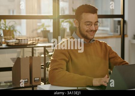 Smiling Man Using Computer in Office Lit By Sunlight Stock Photo
