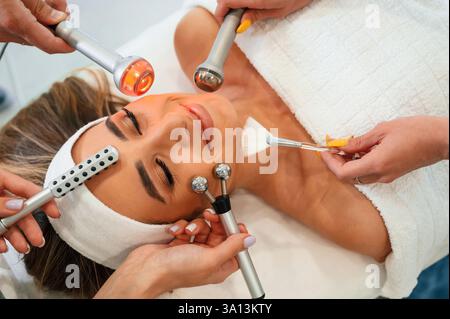 Hands are holding bunch of cosmetitian tools. Woman face getting facial care by beautician hands at spa salon. Stock Photo