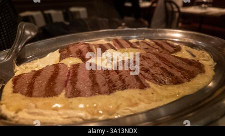 Slices of grilled beef tenderloin resting on a bed of creamy sauce and topped with butter, served on an elegant silver platter in a restaurant setting Stock Photo