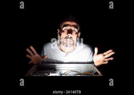 Confused Man Repairing Computer in Dark Stock Photo