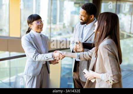 Three professionals in stylish business attire share a friendly handshake while discussing ideas in a bright, contemporary office environment with cit Stock Photo