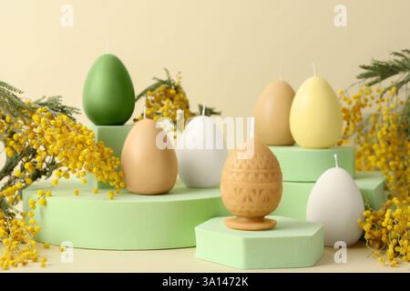Beautiful egg shaped candles and mimosa flowers on beige background. Easter decor Stock Photo
