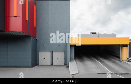 Parking garage entrance. Grey building facade with red trim, two doors and gates for cars leading to on-ramp to higher floors. Stock Photo