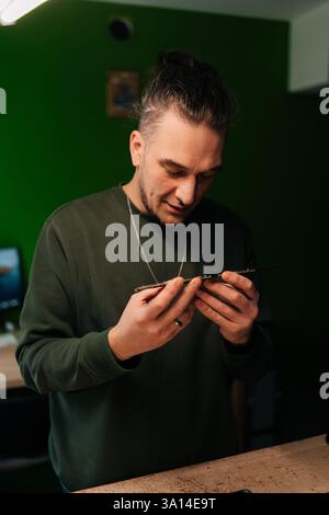 Vertical portrait of professional computer master examining motherboard, troubleshooting issues in professional electronics repair workshop with green Stock Photo