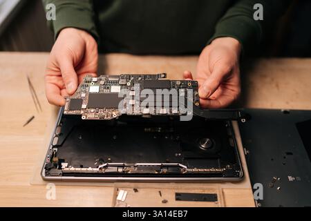 Cropped shot of electronic technician inspecting delicate laptop motherboard component, diagnostic process underway in specialized repair workshop. Stock Photo