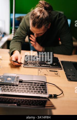 Vertical portrait of technician using tweezers repairing laptop motherboard components in professional electronic workshop setting. Stock Photo
