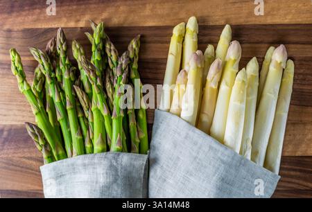 bundle of raw fresh green and white asparagus in grey linen cloth on rustic wood board, top down view Stock Photo