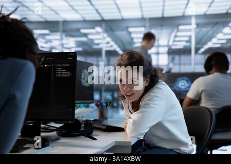 Joyous technician chatting with colleague while doing maintenance on artificial intelligence neural networks. Smiling admin talking with coworker while using AI systems aiding processing Stock Photo